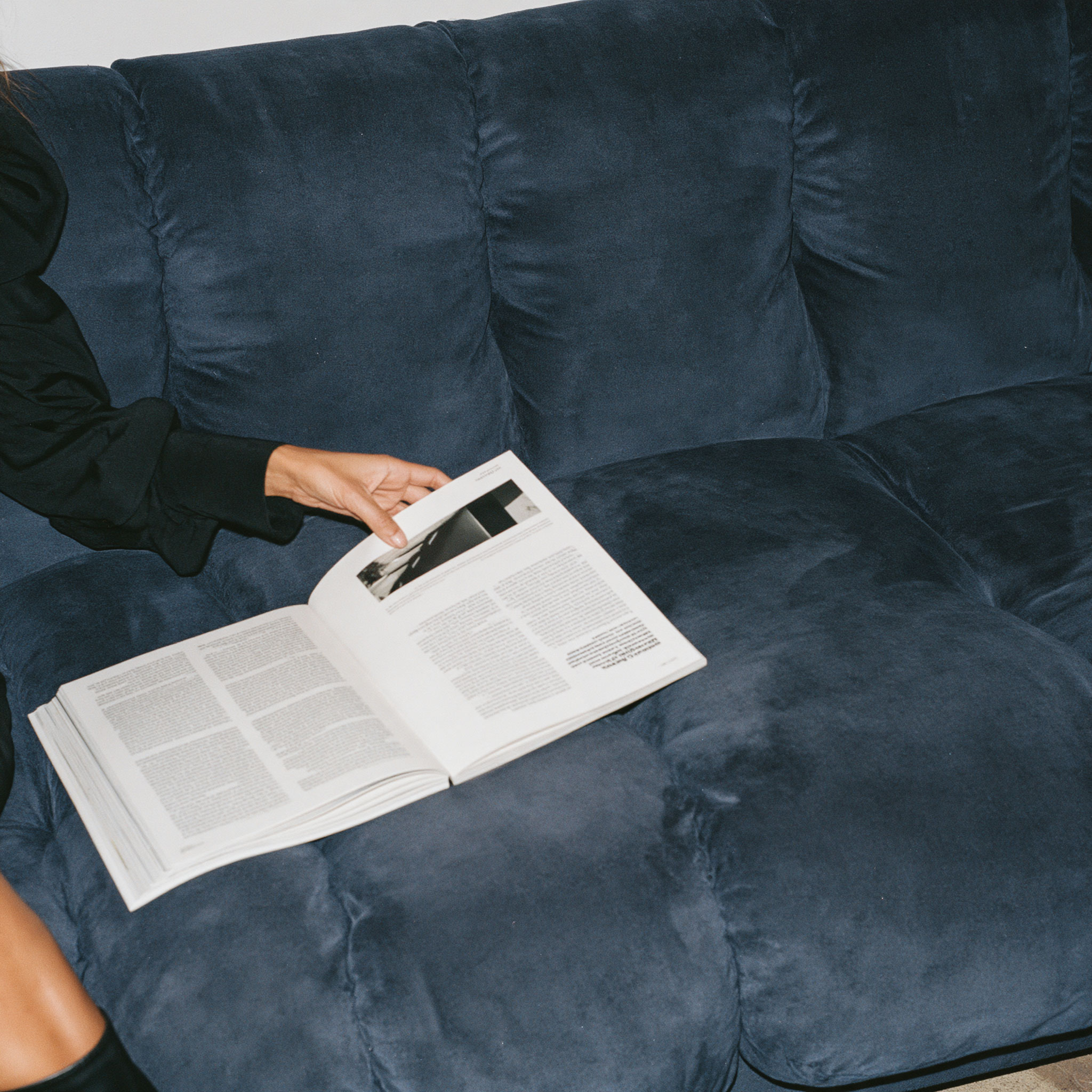 Person holding an open magazine on a navy velvet sofa